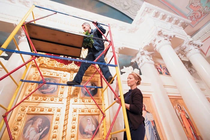  Андрей Максимов и Алена Душка забираются наверх по строительным лесам, чтобы прикрепить цветочные композиции над иконостасом